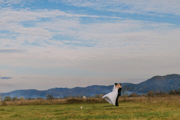 Fototapeta premium A bride and groom are standing in a field, with the bride holding a bouquet. The sky is blue and there are some clouds in the background. Scene is romantic and happy