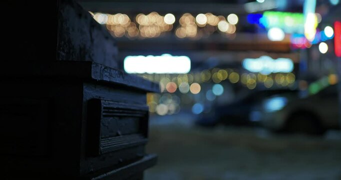 Night city, out of focus. Cars drive along a city street against the background of illuminated storefronts of a large store. Hand held. Siberia.