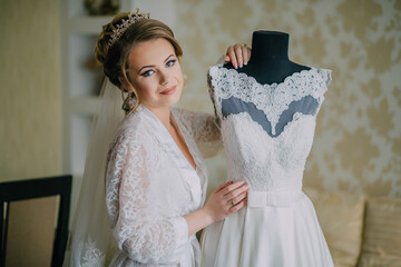 A woman is holding a dress up to her chest. The dress is white and has a lace design. The woman is...