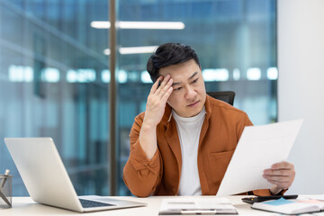 Worried and anxious man doing paperwork inside office, Asian man thinking and reading financial...