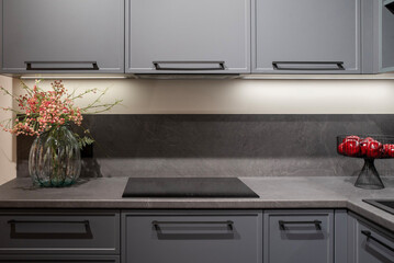 Contemporary kitchen design with grey cabinets, black induction hob, and floral arrangement