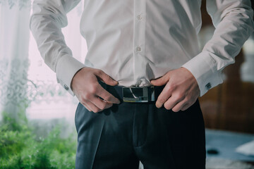 A man is wearing a white shirt and black pants. He is adjusting his belt. Concept of formality and attention to detail