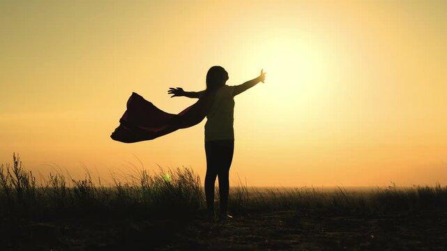 girl superhero with long hair red cape wind sunset. brave superhero ready help. superhero background sky rays sun. childhood dream teenager. child stretches hands sun. happy childhood superhero game.