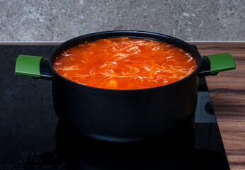 Red vegetable tomato soup with cabbage in black saucepan cook on induction hob