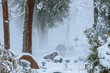 A tranquil winter cemetery during a snowstorm, featuring snow-covered trees, gravestones, and a...