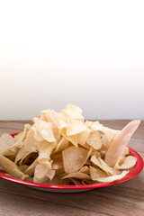 A red plate filled with thinly sliced, crispy cassava chips (keripik singkong) on a wooden table.