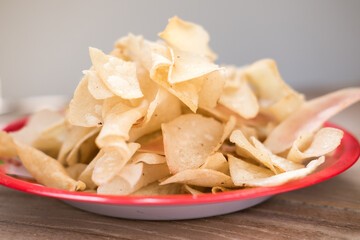 A red plate filled with thinly sliced, crispy cassava chips (keripik singkong) on a wooden table.