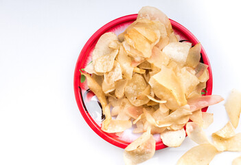 A red plate filled with thinly sliced, crispy cassava chips (keripik singkong) on a white background
