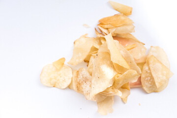 Scattered cassava chips (keripik singkong) on a white surface. The chips are thin, crispy, and have a light golden-brown color with some slightly darker or reddish tinges.