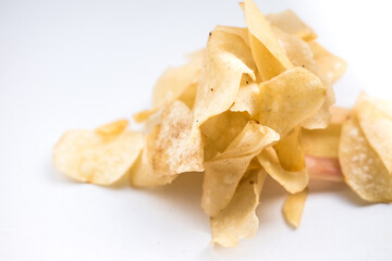 Scattered cassava chips (keripik singkong) on a white surface. The chips are thin, crispy, and have a light golden-brown color with some slightly darker or reddish tinges.