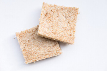 Two slices of whole wheat bread on a white background. The bread has a light brown color and visible texture with small air pockets and bran flecks.