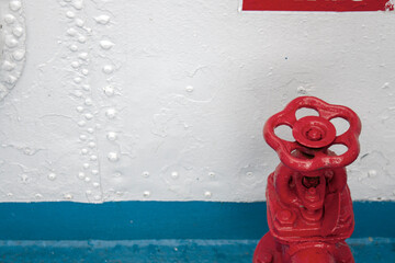 Red water tap on a ship. The white side of the ship with a blue horizontal stripe. White rivets and...