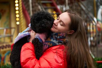 Young woman enjoys a playful moment with her fluffy black dog at a local fair on a chilly day