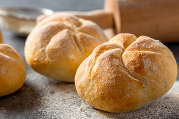 Close-up of freshly baked golden bread rolls with a blurred rolling pin in the background. Bakery...