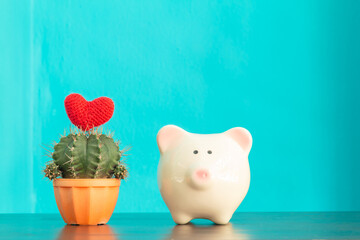 Piggy bank and cactus and red heart put on the top put on the desk on blue wall background, Loan and saving money to health insurance for family concept.