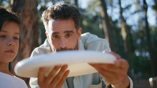Father teaching son throwing frisbee disc at sunny forest closeup. Happy family