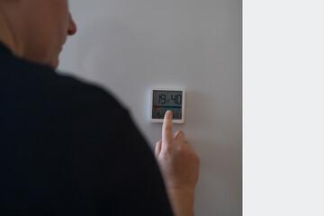 Woman hand lowering the temperature for energy saving. Woman adjusting digital central heating...