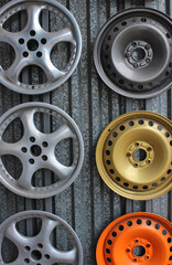 Front parts of steel and light alloy wheel rims of cars on a metal backdrop. Car parts painting...