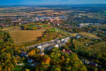 Aerial view of beautiful small town surrounded by fields and forest in autumn season. Bird eye view of village in Poland. Landscape with residential buildings in suburban neighborhood