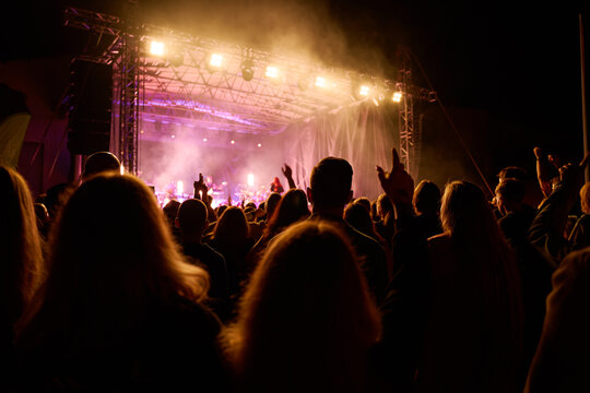 Vibrant live concert scene with band performing on stage under bright spotlights. People enjoying live music performance at an outdoor concert - Powered by Adobe