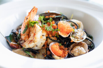 Squid ink spaghetti with garlic, olive oil, chili and seafood on white dish.