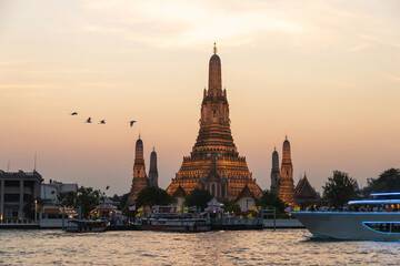 Fototapeta premium Wat Arun Ratchawararam Ratchawaramahawihan (Temple of Dawn) with a tourist on a cruise boat capturing a photo in a magical moment along the Chao Phraya river at twilight in Bangkok, Thailand.