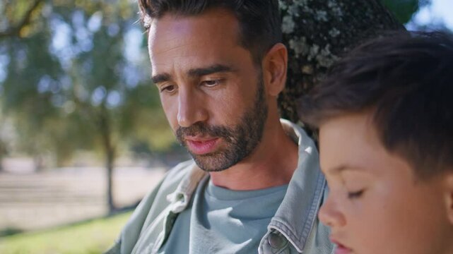 Bearded father talking kid under cozy tree at garden closeup. Boy listening man