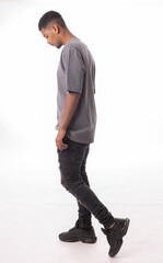 Naklejka premium Young man wearing gray t-shirt and ripped black jeans is walking and looking down