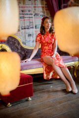 A woman in a red dress sits on a couch in front of a wall covered in Chinese newspapers