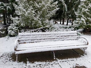 A park bench covered in snow in the middle of a park
