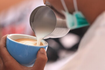 Milk pours into cup creating coffee art by barista.