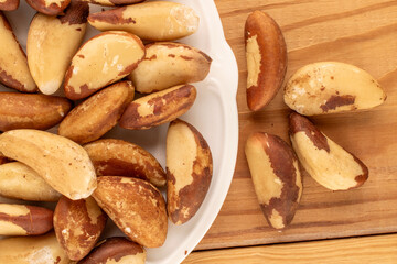 Brazil nuts without shells on a white ceramic plate on a wooden table, close-up, top view.