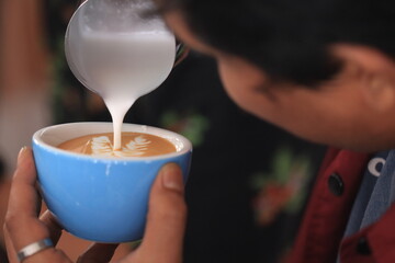 Milk pours into cup creating coffee art by barista.