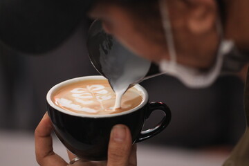 Milk pours into cup creating coffee art by barista.