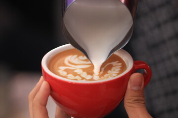 Milk pours into cup creating coffee art by barista. © Aillusionist
