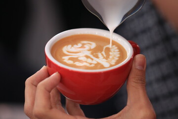 Milk pours into cup creating coffee art by barista.