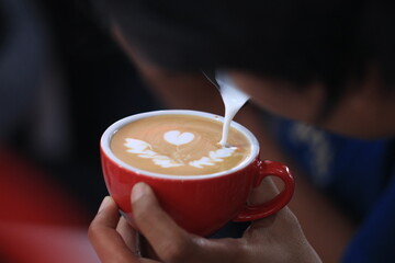 Milk pours into cup creating coffee art by barista.