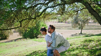 Smiling dad carrying child on grassy lawn. Joyful father holding son at garden