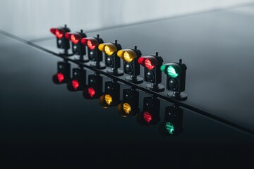 Miniature traffic lights in a row, showcasing red, yellow, and green signals reflecting on a dark surface.