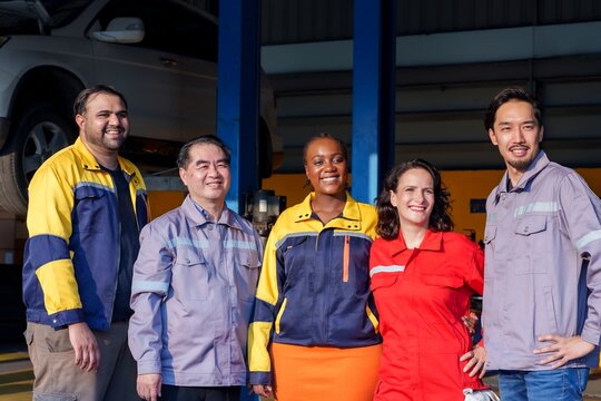 Smiling mechanic holding a power tool while kneeling beside a red car in an auto repair shop. Bright and confident, showcasing expertise and passion for automotive service.