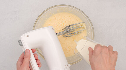 Ingredients like cream cheese, eggs, whipped cream, and powdered sugar mixed with a mixer, flat lay