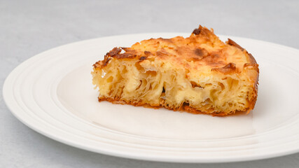 Slice of phyllo dough pie with cream cheese filling close-up on a white plate isolated on a light grey background