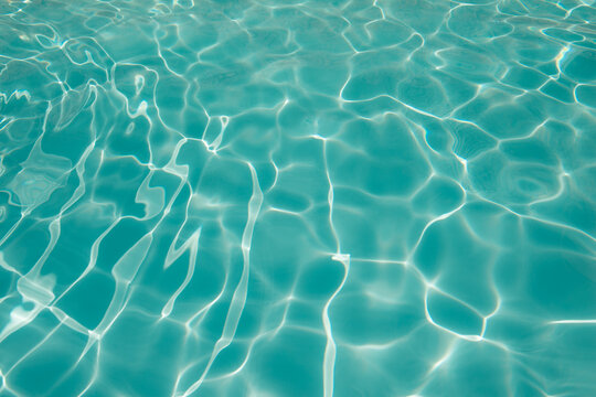 abstract background of clear blue water surface in the swimming pool with ripples and sunlight
