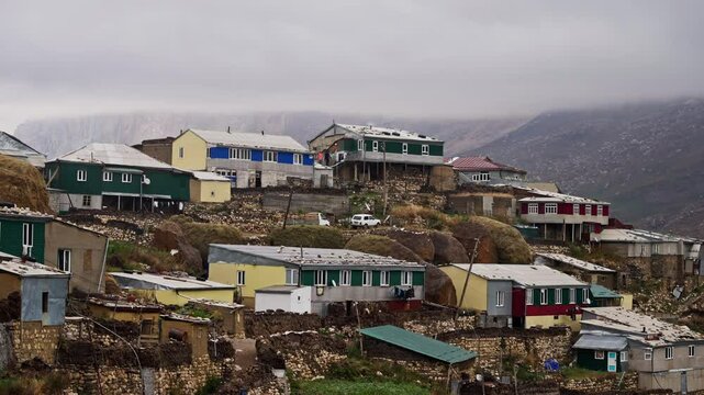 Colorful dwellings clustering mountainous xinaliq village landscape, azerbaijani architecture ascending rocky terrain under overcast mountainous background