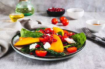 Fresh salad of persimmon, cherry tomatoes, ricotta, spinach and pomegranate on a plate on the table