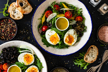 Fresh green salad with vegetables, boiled eggs and vinaigrette sauce on black table