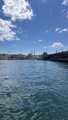 Obraz premium View of the Galata Bridge and Istanbul skyline with the iconic mosque domes and minarets under a bright blue sky and scattered clouds