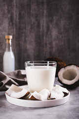 Fresh coconut milk in a glass and coconut pieces on a plate on the table vertical view