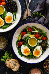 Fresh green salad with vegetables, boiled eggs and vinaigrette sauce on black table