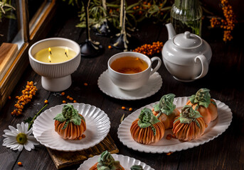 Pumpkin shaped desserts with tea and lit candle creating cozy autumn atmosphere